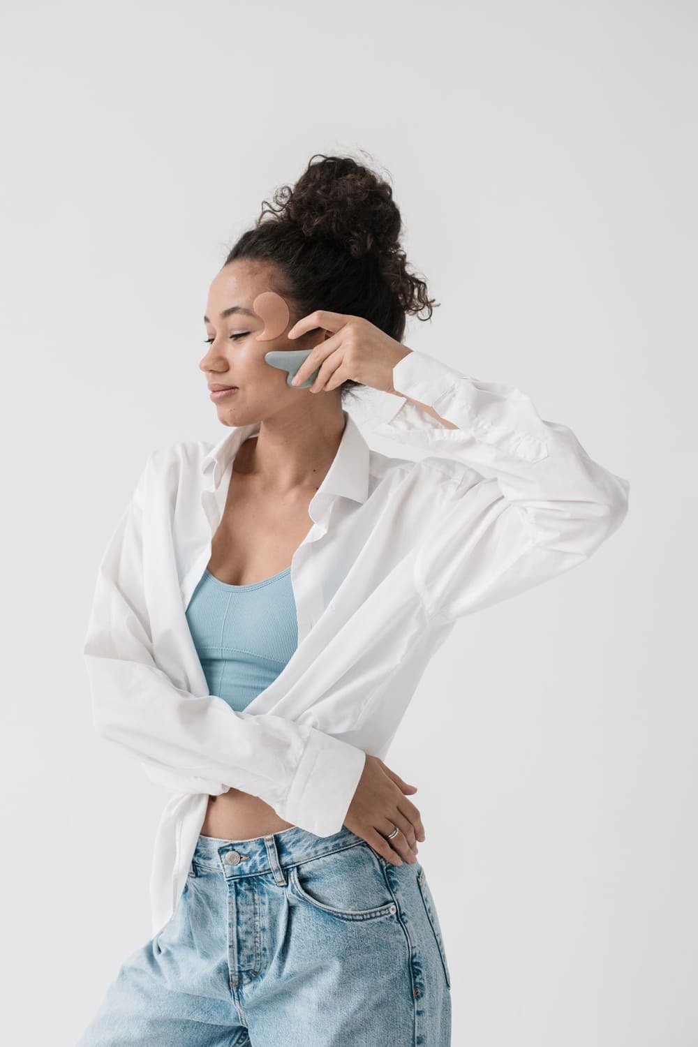 A woman in a white shirt gliding a gua sha stone along her cheek